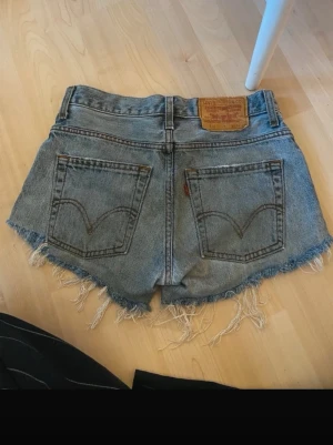 Levi's jeansshorts med fransig kant - Klassiska blå jeansshorts från Levi's med rå, fransig kant och femficksmodell. Shortsen har normal passform och bälteshällor. Perfekta för sommaren och har den ikoniska Levi's-lappen bak i midjan.