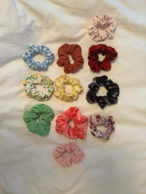 11-pack scrunchies i olika färger - Säljer ett set med 11 scrunchies i olika färger och mönster. Inkluderar bland annat blommigt, rutigt, enfärgat och sammet i nyanser som röd, grön, blå, gul, rosa och lila. Perfekt för att piffa till håret med en färgklick eller matcha med olika outfits.