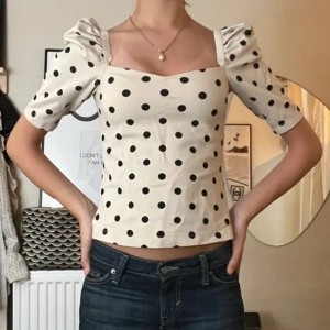 Prickig topp  - Supersöt topp från H&M med puffärmar och fyrkantig urringning. Vit botten med svarta prickar, croppad passform och lätt stretchigt bomullsmaterial. Perfekt för dig som gillar trendiga detaljer och en feminin look.