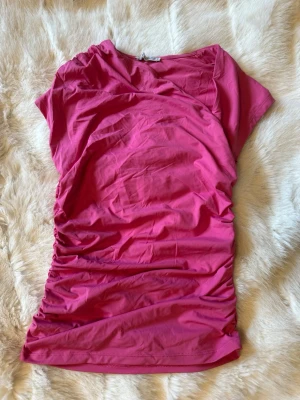 Rosa ruched topp med kort ärm - Snygg rosa topp med kort ärm och rynkade sidor. Perfekt att styla med jeans eller kjol för en trendig look. Använd 1 gång! 