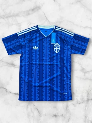 Blå Sverige matchtröja Adidas - Säljer en blå matchtröja från Adidas med Sveriges landslagsemblem på bröstet. Tröjan har ett unikt mönster i olika blå nyanser, vita Adidas-ränder på axlarna och V-ringad hals. Tillverkad i lätt och ventilerande material, perfekt för fotboll eller träning.