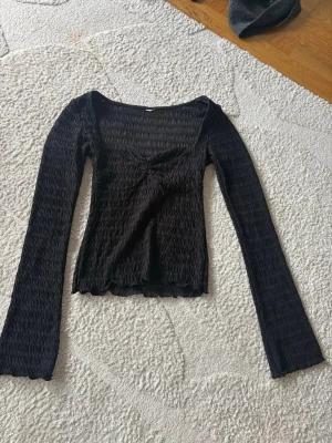 Svart ribbad långärmad topp - Säljer en svart ribbad topp med lång ärm och lätt croppad passform. Toppen har en söt v-ringning och stretchigt material som sitter skönt, jag har klippt av lappen för den kliade 