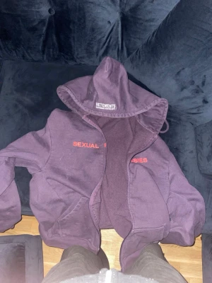 Lila hoodie från Vetements - Säljer en lila hoodie från Vetements med trycket 'SEXUAL FANTASIES' i rött på bröstet. Hoodien har en stor huva, lång ärm och en relaxed passform. Tillverkad i mjuk bomull som känns skön mot huden. Perfekt för dig som gillar streetwear och statement-plagg. Fläckar fram på tröjan går att få bort.  Väldigt oversized. Medium.
