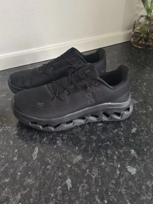 Svarta On Cloudmonster sneakers - Säljer ett par helsvarta On Cloudmonster sneakers med chunky sula och ventilerande meshmaterial. Skorna har en unik, hålig mellansula för extra dämpning och cool look. Klassisk låg modell med snörning och diskreta loggor på sidan.