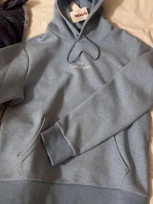 Ljusblå hoodie från Polo Ralph Lauren - Knappt använd kanske 7 gånger, Snygg ljusblå hoodie från Polo Ralph Lauren med broderad logga på bröstet och ärmen. Klassisk känguruficka framtill och justerbar huva med dragsko. Tillverkad i mjukt bomullsmaterial som känns skönt mot huden. Perfekt för en avslappnad och trendig look.