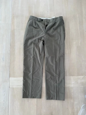 Bruna kostymbyxor i rak modell - Snygga  kostymbyxor med rak passform och pressveck. Byxorna har knapp och dragkedja fram samt bälteshällor i midjan. Tillverkade i ett slätt tyg som ger en clean look. Perfekta för dig som vill ha en stilren och enkel byxa.