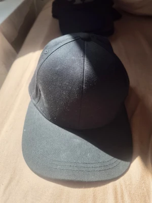 Svart klassisk keps H&M - En stilren svart keps med böjd skärm och sex paneler. Kepsen är helt utan logga eller tryck och har en enkel, clean design. Tillverkad i ett mjukt tygmaterial som känns bekvämt på huvudet. Perfekt för dig som gillar minimalistisk stil.