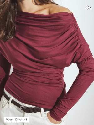 Soft Line långärmad draperad topp - Slut i butiken! Trendig vinröd offshoulder topp med långa ärmar och draperad effekt över bröstet och axlarna. Sitter tight och har en snygg asymmetrisk halsringning som visar ena axeln. Perfekt att styla med höga jeans eller kjol.
