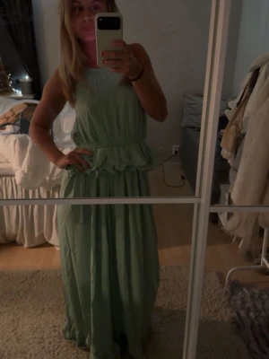 Ljusgrön långklänning med volang - Snygg ljusgrön långklänning med volangdetalj i midjan och ärmlös design. Perfekt för sommarens alla tillfällen. Klänningen har en avslappnad passform och är tillverkad i ett lätt material som känns svalt och bekvämt. Prislappen kvar och aldrig använd därav priset, säljer då jag inte tyckte om mig själv i färgen 