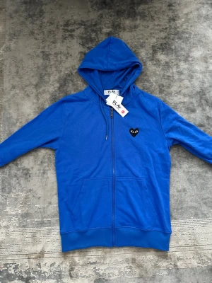 Blå hoodie (läs bio) - Snygg blå hoodie med dragkedja från Comme des Garçons Play. Åker utomlands den 20/6 så skynda på!