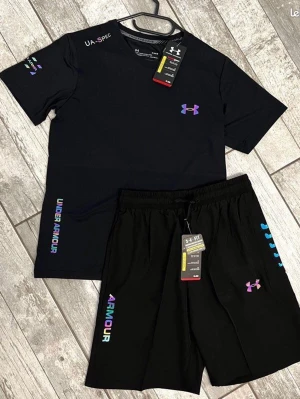 Svart träningsset FÖRBESTÄLLING ENDAST  - Snyggt svart träningsset från Under Armour med t-shirt och shorts. Setet har färgglada loggor och textdetaljer i lila, blått och rosa. Tillverkat i ett lätt och snabbtorkande material som passar perfekt till gymmet eller löpning. Helt nya, fraktar inom 24 timmar 