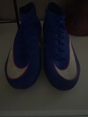 Nike Air Zoom blå fotbollsskor - Säljer ett par Nike Air Zoom fotbollsskor i blått med vit och rosa swoosh. Skorna har högt skaft för extra stöd och snörning framtill. Perfekta för dig som vill ha bra grepp och snygg design på planen.