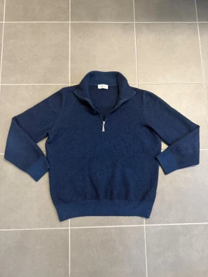 Mörkblå halvzip-tröja från Gran Sasso, stl XS - Mörkblå stickad tröja från Gran Sasso med halv dragkedja och hög krage. Tröjan har ribbade muddar och nederkant, perfekt för lager-på-lager. Tillverkad i mjukt material som ger en stilren och klassisk look.