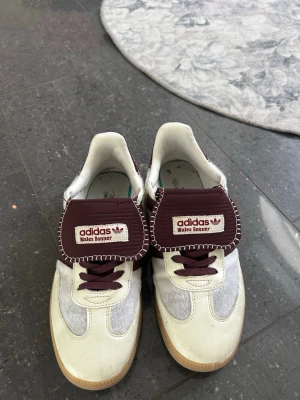 Adidas Wales Bonner sneakers vinröd/vit - Snygga Adidas Wales Bonner sneakers i vitt och vinrött med kontrastsömmar och breda tungor. Skorna har klassisk låg siluett, vita och grå paneler i mocka och läder samt vinröda detaljer och snören. Perfekta för dig som gillar unika samarbeten och streetwear.