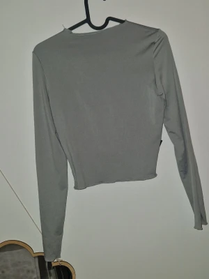 Långärmad topp - Säljer en enkel och stilren grå långärmad topp som går att använda både bak som fram. Toppen har en fin passform, rund halsringning och är tillverkad i mjuk bomullsmix. Perfekt att matcha med jeans eller kjol för en clean look.
