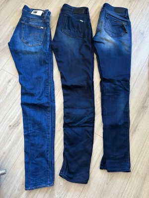 Blå jeans från G-Star RAW - Säljer tre par blå jeans från G-Star RAW med klassisk femficksdesign och snygga detaljer på bakfickorna. Jeansen har raka ben och olika nyanser av blått med lätt slitning. 