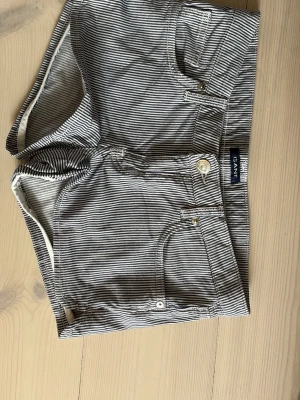 Randiga shorts från Gant - Lågmidjade randiga shorts från Gant. Klassisk femficksmodell med knapp och dragkedja framtill. Shortsen har bälteshällor och är tillverkade i ett mjukt bomullsmaterial. Perfekta för varma dagar! De är i nyskick utan skador. Väldigt sköna och trendiga. Ganska små i storleken