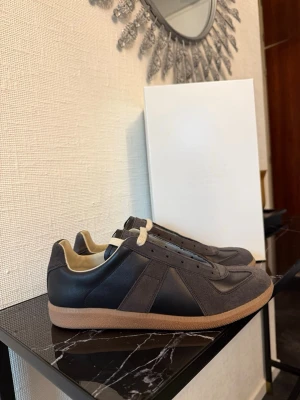 Svarta sneakers från Maison Margiela - Maison Margiela sneakers i svart läder och mocka med beige innersida och gummisula. Klassisk design med rund tå och diskreta detaljer. Perfekt för dig som gillar stilrena och trendiga skor.