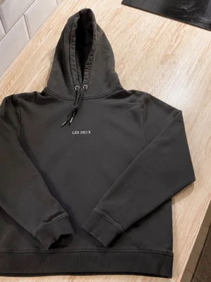 Mörkgrön hoodie från Les Deux - Snygg mörkgrön hoodie från Les Deux med broderad logga på bröstet. Klassisk känguruficka framtill, ribbade muddar och justerbar huva med snören. Perfekt för en avslappnad och stilren look.
