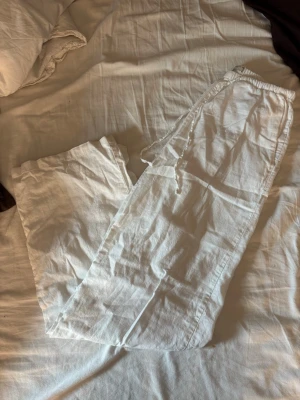 Vita linnebyxor från Gina Tricot - Säljer ett par vita linnebyxor från Gina Tricot i storlek XS. Byxorna har resår i midjan och dragsko för skön passform. Tillverkade i ett lätt och luftigt linnematerial, perfekta för varma dagar. Klassisk rak modell som är enkel att styla.