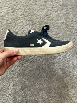 Converse CONS svarta låga sneakers - Snygga Converse CONS sneakers i marinblå mocka med vita detaljer och klassisk stjärnlogga på sidan. Skorna har vita sulor och marinblåa skosnören. Perfekta för en avslappnad streetwear-look och passar till det mesta i garderoben.