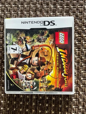 LEGO Indiana Jones DS-spel - Nintendo DS-spelet LEGO Indiana Jones: The Original Adventures. Omslaget har färgglada LEGO-figurer och äventyrstema med Indiana Jones i fokus. Spelet är från LucasArts och rekommenderas från 7 år. Perfekt för dig som gillar action och pussel i LEGO-världen.