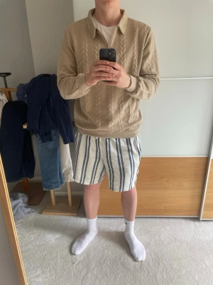 Beige stickad tröja med dragkedja - Helt ny och oanvänd schysst beige stickad tröja med halv dragkedja och krage. Tröjan har ett flätmönster framtill och ribbade muddar vid ärmslut och nederkant. Perfekt för lager på lager och en avslappnad men trendig look och perfekt på en sval sommarkväll