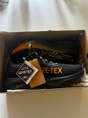 ASICS GT-2000 14 GORE-TEX löparskor - Säljer ett par svarta ASICS GT-2000 14 löparskor med GORE-TEX-material som håller dig torr. Skorna har vita och gula detaljer, klassisk snörning och slitstark sula. Perfekta för löpning i alla väder och har en sportig, modern look. Ny pris 1500kr