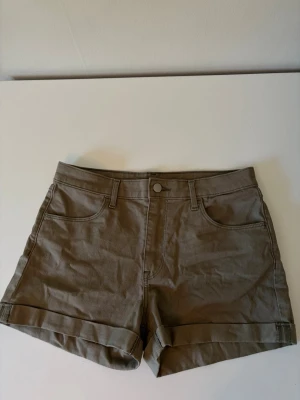 Beige bomullsshorts med uppvik - Snygga beige shorts i bomull med uppvikta benslut och klassisk femficksdesign. De har normal passform och stängs med knapp och dragkedja. Perfekta för varma dagar och enkla att matcha med olika stilar.