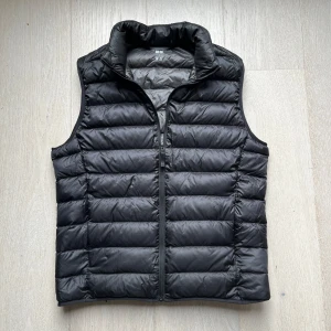 uniqlo väst - Svart, quiltad dunväst från Uniqlo Ultra Light Down. Västen är superlätt, har hög krage och dragkedja framtill. Tillverkad i syntetmaterial med dunfyllning och kommer med en smidig förvaringspåse. Perfekt för lager-på-lager och enkel att ta med sig. skriv vid minsta fråga!