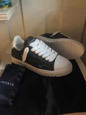 Svarta och vita sneakers från Numeris - Snygga sneakers från Numeris med svart slitstarkt tyg och vita detaljer. Skorna har tjock vit sula, vita skosnören och en cool kontrast mellan material och färg. Märkeslogga på plösen och trendig streetwear-vibe. Perfekta för dig som gillar stilrena men ändå unika sneakers.
