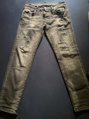 Grå slitna skinny jeans - Säljer ett par grå svart dsquared  jeans med slitningar och hål på både fram- och baksida. Jeansen har fem fickor, knappgylf och en cool, tvättad look. Perfekta för dig som gillar en edgy och avslappnad stil.