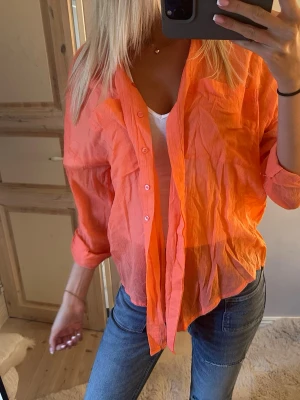 Orange transparent skjorta med knappar - Säljer en tunn och transparent orange skjorta med knappar framtill. Skjortan har lång ärm och är tillverkad i ett lätt material som ger en avslappnad vibe. Perfekt att styla över ett linne eller t-shirt för en cool lager-på-lager-look.