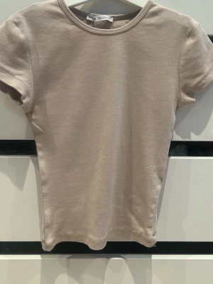 Beige kortärmad t-shirt från Bershka - Säljer en enkel och stilren beige t-shirt från Bershka i storlek XS. T-shirten har rund halsringning och korta ärmar. Tillverkad i mjuk bomull som känns skön mot huden. Perfekt basplagg att matcha till allt.