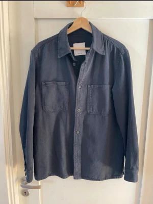 Mörkblå overshirt från Mango - Stilren mörkblå overshirt från Mango som är perfekt för kyligare sommarkvällar. Overshirten har klassisk krage, raka ärmar och är tillverkad i ett mjukt bomullstyg. Perfekt att slänga över en t-shirt för en avslappnad look. 