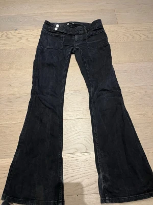 Svarta bootcut jeans med strass - Säljer ett par svarta bootcut jeans med låg midja och snygga strassdetaljer på bakfickorna. Jeansen har två framfickor och två bakfickor med dekorativa mönster. Perfekta för dig som gillar en unik och trendig look.