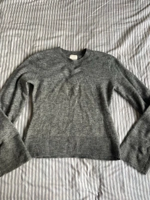 Grå stickad tröja från H&M - Mysig grå stickad tröja från H&M med rund halsringning och ribbade utsvängda armar. Tröjan har en enkel och stilren design som passar perfekt till jeans eller kjol. Materialet är mjukt och bekvämt för kalla dagar.
