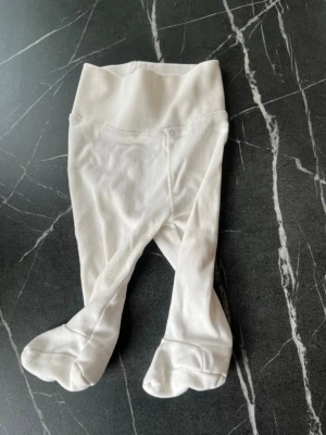 Vita babystrumpbyxor från H&M - Mjuka vita strumpbyxor för baby från H&M, tillverkade i ekologisk bomull. Modellen har fot och bred resår i midjan för extra komfort. Perfekta för de allra minsta, storlek 0-1 månad.