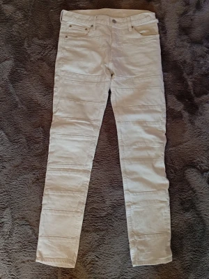 Beiga skinny jeans med detaljer - Snygga jeans med horisontella sömdetaljer över benen och klassisk femficksdesign. Jeansen har normal midja, bälteshällor och stängs med knapp och dragkedja. Perfekta för en clean och stilren look. Finns ett hår på vänster sidan bak som syns i bild fyra därför det låga priset 