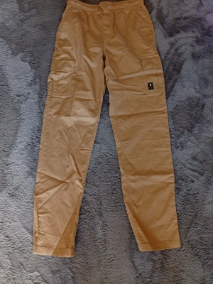 Beige cargobyxor  - Snygga beige cargobyxor med flera praktiska fickor på sidorna och elastisk midja. Byxorna har en avslappnad passform och är tillverkade i ett mjukt bomullsmaterial. Perfekta för en casual och trendig stil. Dom finns på kids brandstore för 450 jag säljer dom för 400 för dom endast är provade 