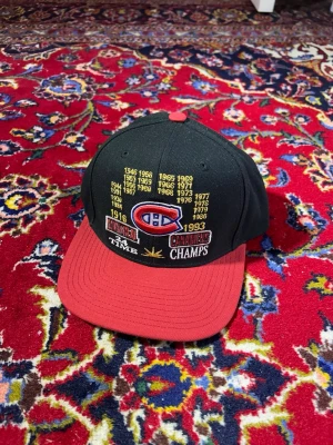 Montreal Canadiens keps Mitchell & Ness - Snygg Montreal Canadiens keps från Mitchell & Ness med svart krona och röd skärm. Broderade mästerskapsår och lagets logga framtill, samt broderad Mitchell & Ness-text bak. Justerbar snapback och klassisk form. Perfekt för hockeyfans!