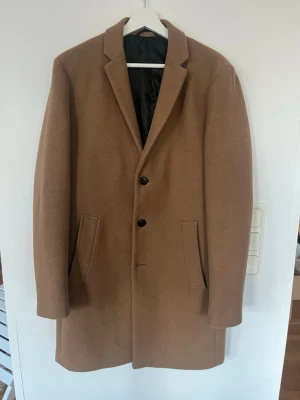 Beige rock - Säljer en stilren beige rock med tre knappar framtill och två snedställda fickor. Rocken har rak passform, krage med slag och är fodrad med svart innerfoder. Perfekt för dig som vill ha en tidlös och elegant look. 