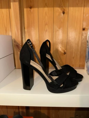 Svarta chunky pumps från Anna Field - Snygga svarta pumps från Anna Field med bred klack och platåsula. Skorna har korsade remmar över foten och justerbart spänne vid ankeln. Tillverkade i mockaimitation som ger en trendig och stilren look.