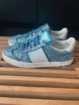 Blå glittriga sneakers med vita detaljer - PRIS KAN DISKUTERAS❣️ Snygga Valentino sneakers med blå glitteryta, blå skosnören och vita paneler på sidorna. Skorna har vit sula och insida, samt metallicblå plös. Perfekta för dig som vill sticka ut med lite extra bling i vardagen. 