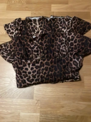 Leopardmönstrad off shoulder topp - Säljer en trendig off shoulder topp med leopardmönster i bruna och svarta toner. Toppen har puffiga ärmar och smockad midja som ger en snygg siluett. Perfekt för dig som vill sticka ut med ett djurmönstrat plagg.