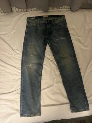 Blå tapered jeans från Weekday - Säljer ett par blå tapered jeans från Weekday med slitningar och tvättad look. Jeansen har fem fickor, normal midja och smalare ben. Perfekta för en avslappnad och trendig stil.