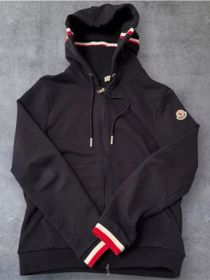Navy Moncler zip hoodie - Navy Moncler zip hoodie med röd/vit/blå mönster i slutet av armarna och på luvan. Helt ny, skick: 10/10. Storlek: S.
