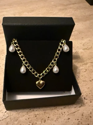 Guldigt halsband 6 mm brett med hjärthänge - Matchande örhängen finns i en separat annons. Finns även i rostfri variant.  Material: 14K guldplätering på rostfritt stål Bredd: 6 mm Längd: 42 + 8 cm (justerbar) Övrigt: Nickelfritt och handgjort Märke: Diavansa smycken