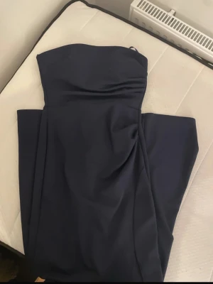 Marinblå axelbandslös långklänning - Elegant marinblå långklänning med axelbandslös design och draperad detalj framtill. Perfekt för dig som vill ha en stilren och klassisk look. Klänningen har en smickrande passform och är enkel att styla med accessoarer.