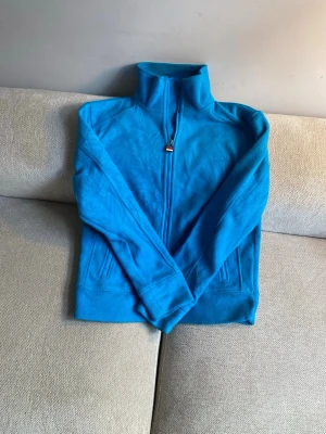 Blå zip hoodie med hög krage - Snygg blå hoodie med dragkedja framtill och hög krage. Tröjan har långa ärmar och två fickor på sidorna. Perfekt för dig som gillar en enkel men stilren look. Materialet är mjukt och bekvämt, bomull eller fleece.